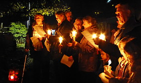 Alte und junge Gemeindemitglieder singen bei Kerzenschein im Dunkeln
