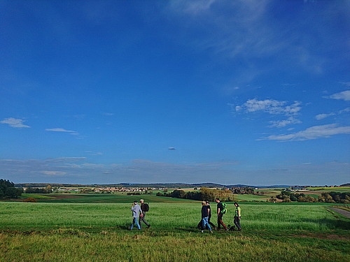 Wandernde Gemeindemitglieder vor sonniger grüner Wiese unter blauem Himmel